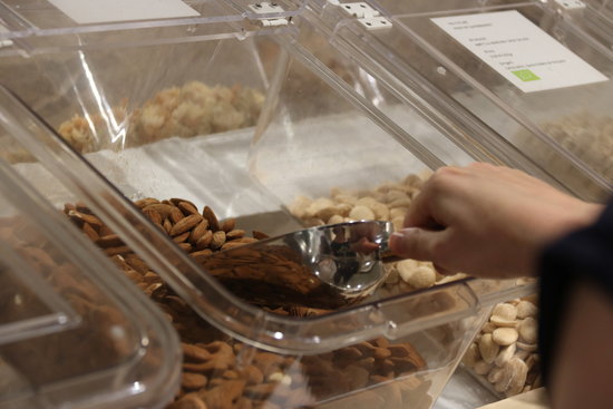 Una mà agafant fruits secs d'un recipient al supermercat Yes Future al barri de Sant Antoni | ACN