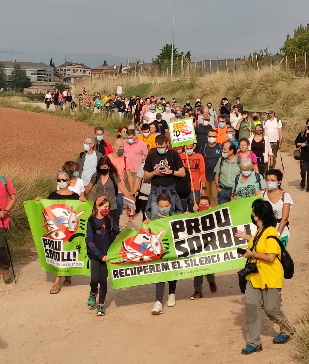 Pla general dels assistents caminant cap a l'aeròdrom de Sant Fruitós de Bages., amb la pancarta en primer terme. Imatge publicada el 3 d'octubre de 2021 (Vertical)