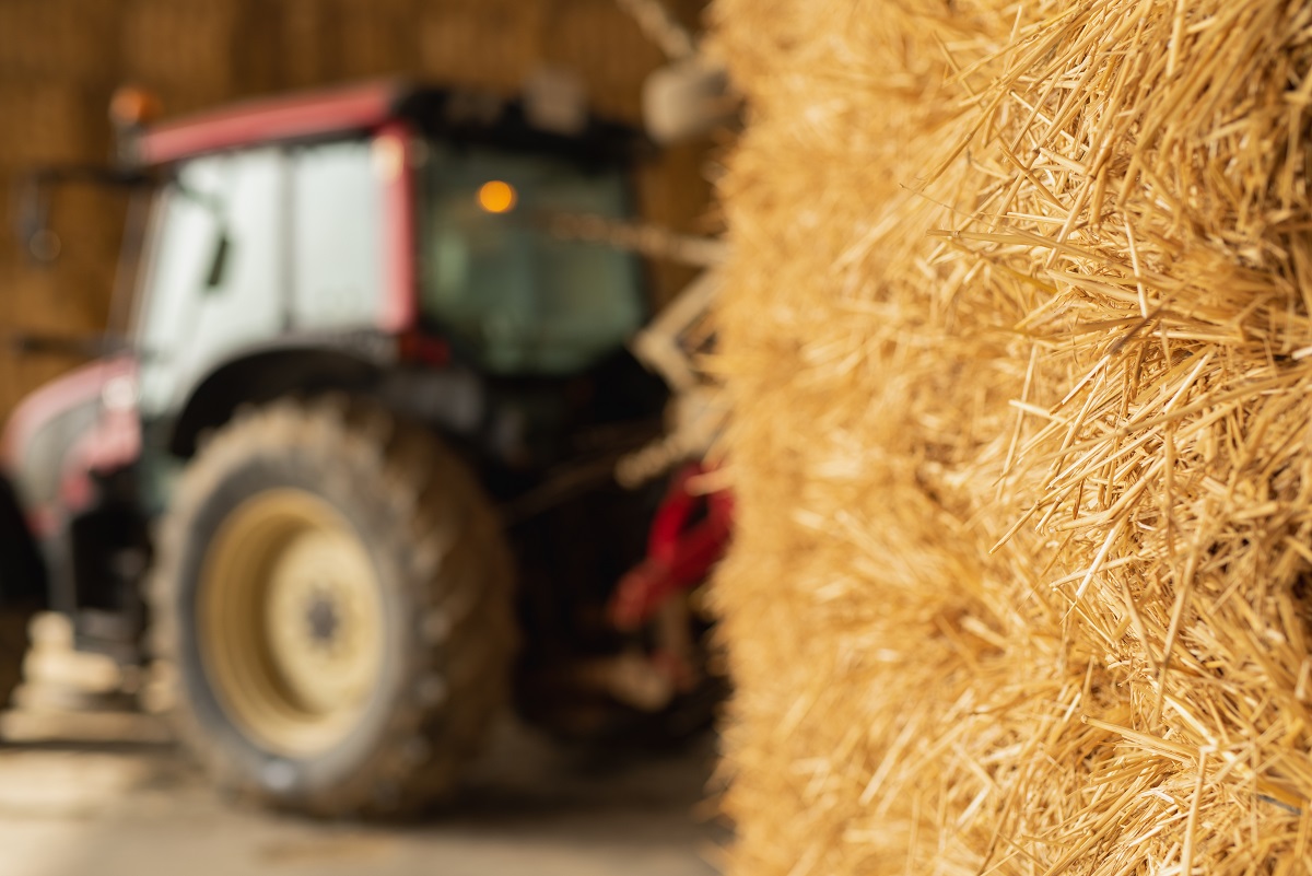 Imatge d'una bala de palla amb un tractor al fons, en una imatge d'arxiu. (Horitzontal)